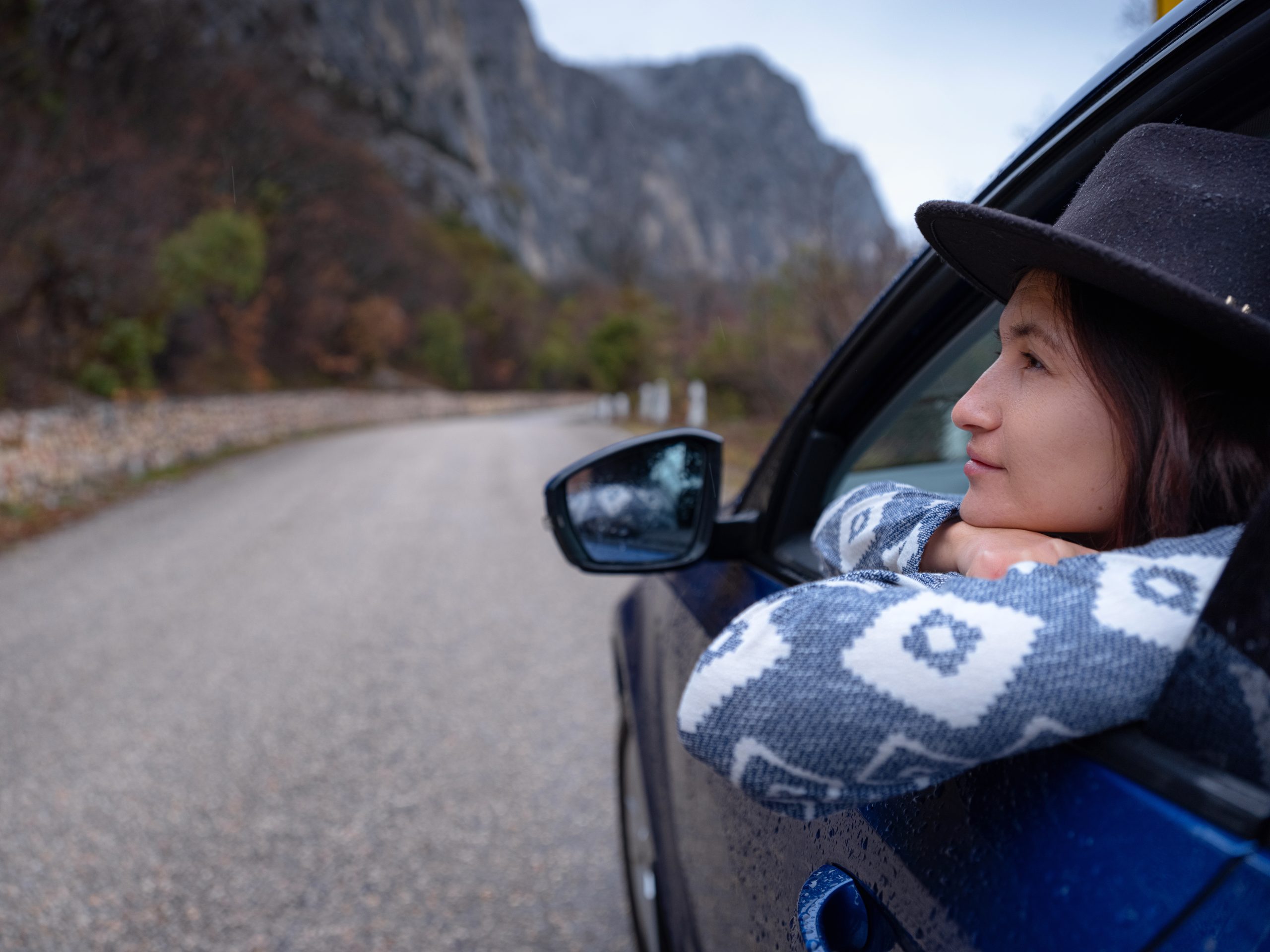 Asian young hipster woman traveling on car vacation. Autumn drive. The rain is falling. The concept of freedom of movement. Fall weekend in the mountains.